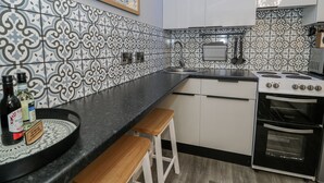 A kitchen with patterned tiles, a stove, oven, sink, and wooden stools. - Estuary Escape (Porthmadog)