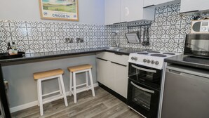 A kitchen with a stove, oven, two stools, and a microwave. - Estuary Escape (Porthmadog)