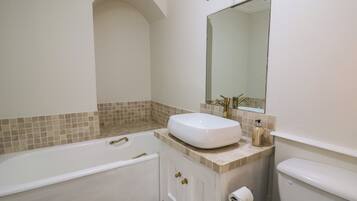 Une salle de bain avec une baignoire blanche, un lavabo avec un miroir au-dessus, et des toilettes.