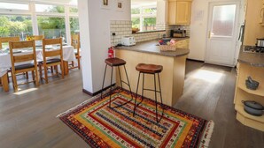 A modern kitchen with a central island, wooden bar stools, and a dining area with a table set for two. - Craggy View (Kendal)