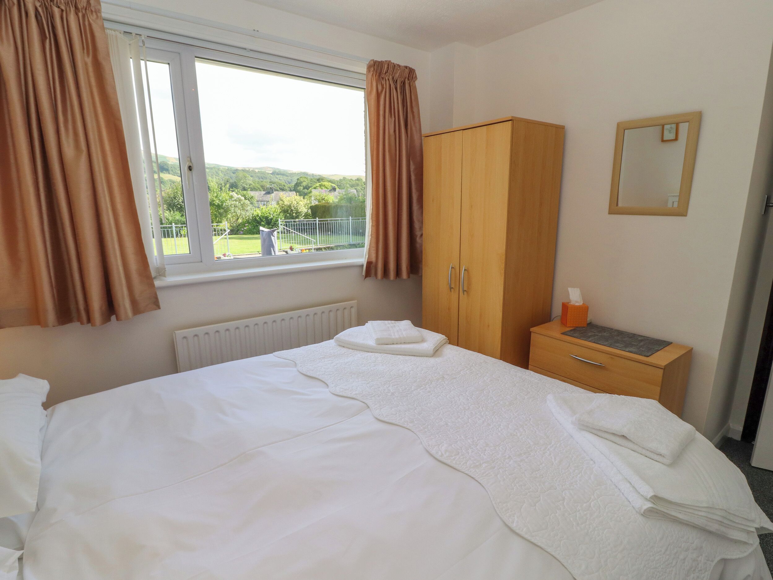 A bedroom with a bed, a wardrobe, a radiator, a window with curtains, and a small table with a tissue box.