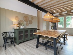 A dining area with a wooden table and chairs, a green cabinet with woven baskets, and a wall decorated with woven placemats. - Rowan Cottage - Fold Yards (Matlock)