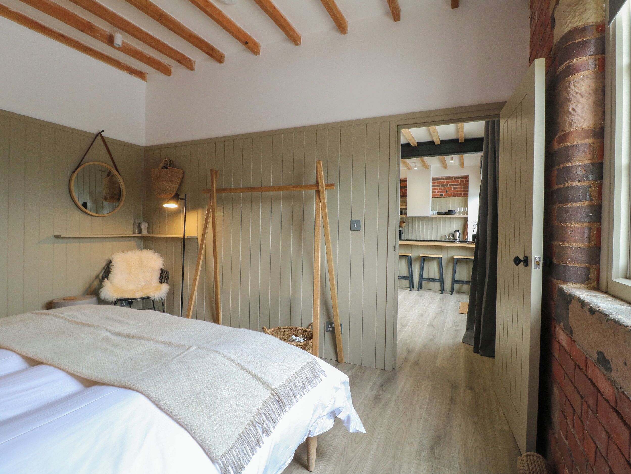 Una camera da letto con un letto, una scala in legno, uno specchio e vista su una zona cucina con sgabelli e una parete in mattoni.