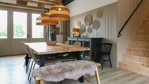 A dining area with a wooden table, wicker chairs, a bench, and a hanging light fixture. - Rowan Cottage - Fold Yards (Matlock)