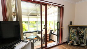 Une pièce avec un téléviseur posé sur un meuble blanc, une porte vitrée donnant sur un espace extérieur avec une table et des chaises, et un buffet avec des portes vitrées.