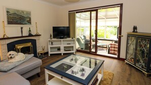 Un salon comprenant un canapé, une table basse avec un plateau en verre, une cheminée, un téléviseur et une porte-fenêtre coulissante donnant sur une terrasse.