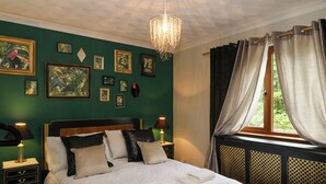 Un lit bien fait, avec du linge de lit blanc et des serviettes pliées, un lustre, des œuvres d’art encadrées accrochées aux murs et une fenêtre avec des rideaux.