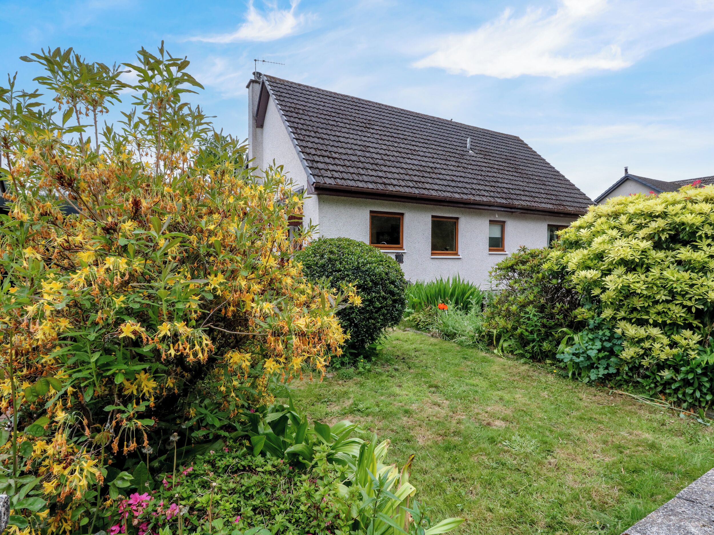 Una casa con techo inclinado, un jardín cuidado y un cielo despejado.