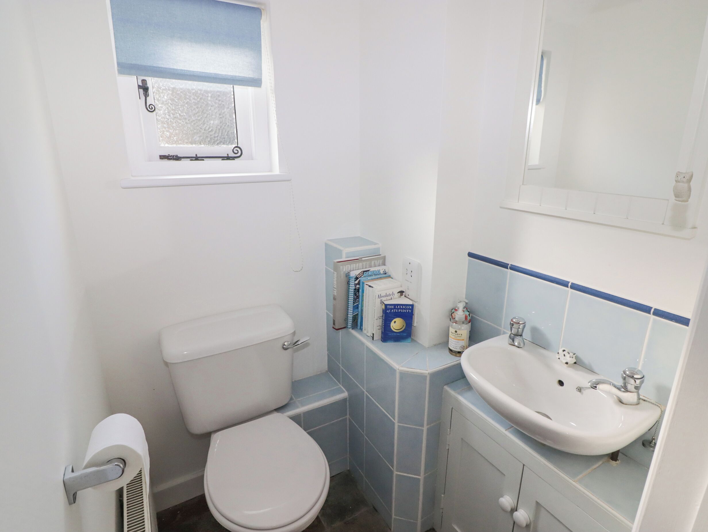 A small, clean bathroom with a toilet, sink, and a window with a blue blind.