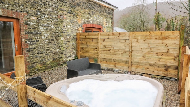 A stone building with a wooden fence, a hot tub, and a chair. - Field View (Llanybydder)