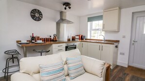 A compact living space with a kitchenette, a sofa with striped cushions, a dining table with chairs, and a window providing natural light. - Field View (Llanybydder)