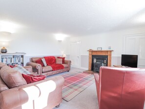 A living room with a sofa, armchair, fireplace, television, and bookshelf. - Fuchsia Cottage (Fortrose)