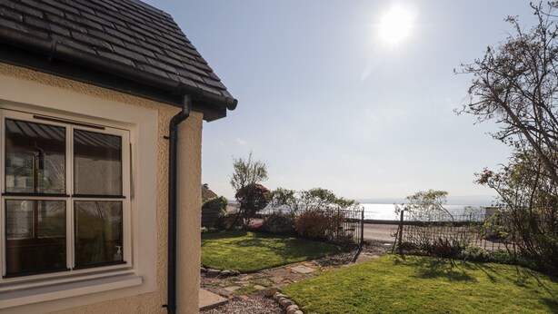 A house with a view of the sea, a gravel path, and a grassy lawn. - Fuchsia Cottage (Fortrose)