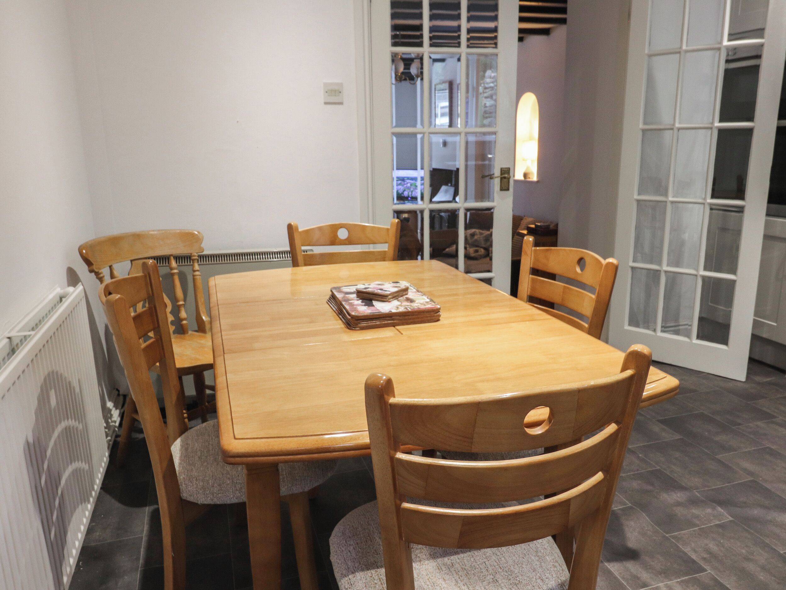 A dining area with a wooden table and chairs, a radiator, and a door leading to another room.