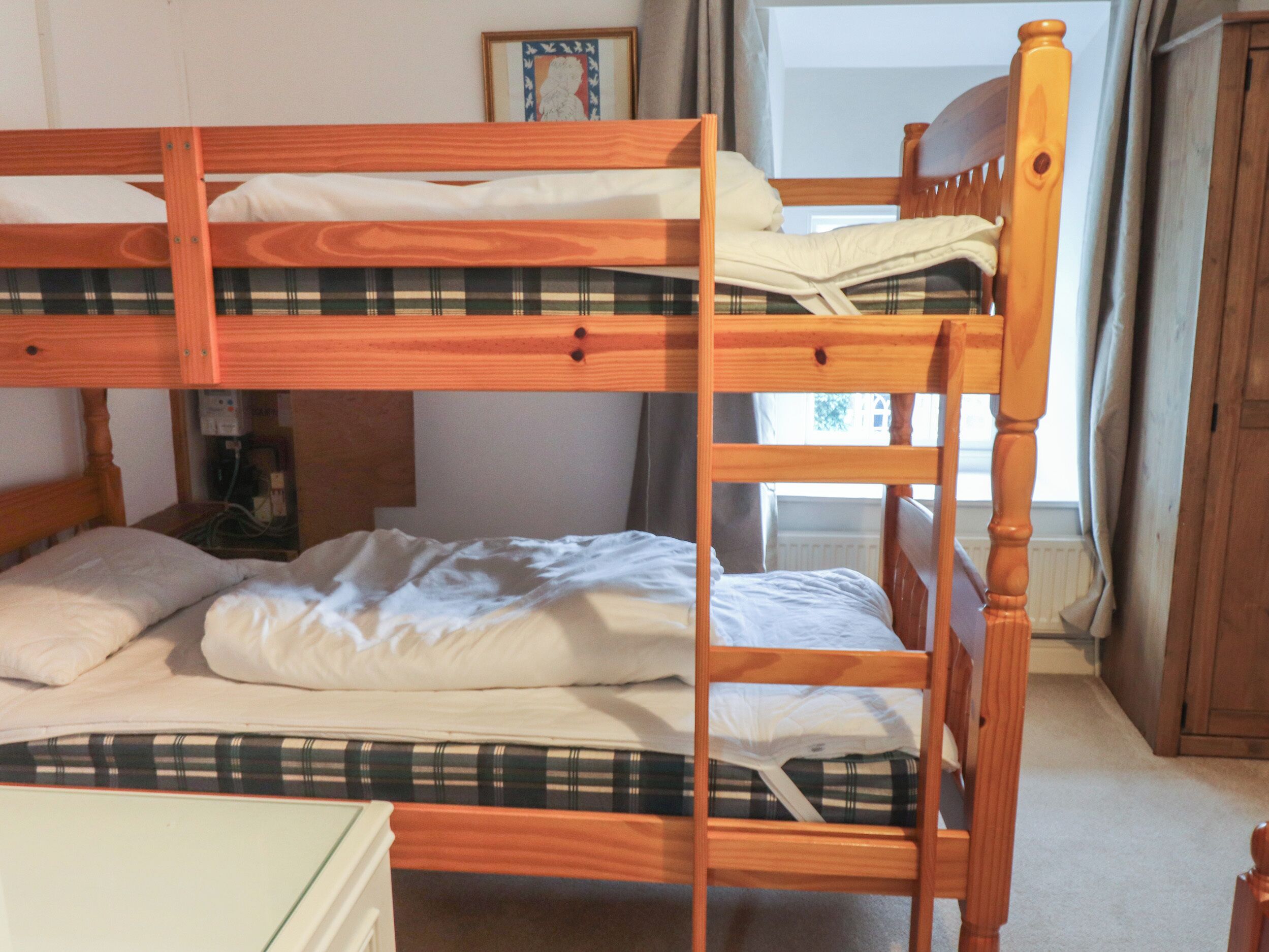 A bunk bed with a plaid-patterned mattress, a wooden headboard, and a small bedside table with a lamp.
