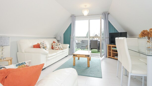 A modern living room with a white sofa, a dining table, and a TV. - 24 Valley Lodge (Gunnislake)