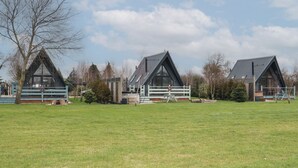 A row of three modern, triangular-roofed cabins with large windows, set in a grassy field with a clear sky. - Sunflower Lodge (Doncaster)