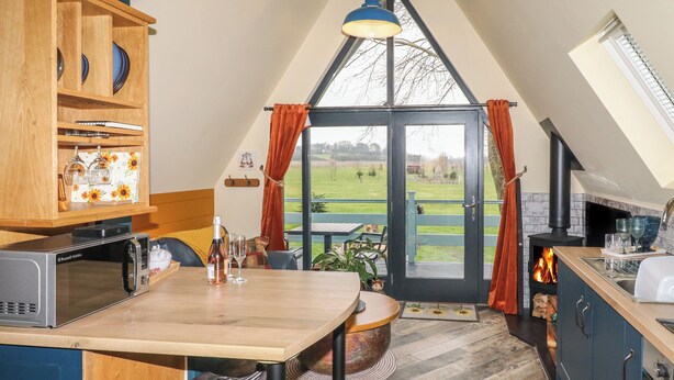 A kitchen with a wooden table, a microwave, and a view of a green landscape through a glass door. - Sunflower Lodge (Doncaster)