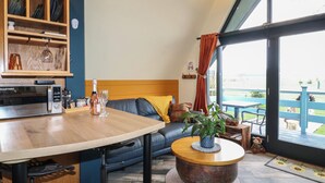 A modern living room with a wooden dining table, a sofa, a coffee table, and a view of the outdoors through large windows. - Sunflower Lodge (Doncaster)
