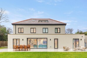 Een huis met twee verdiepingen, een plat dak, grote schuifpuien en een terras met tuinmeubilair.