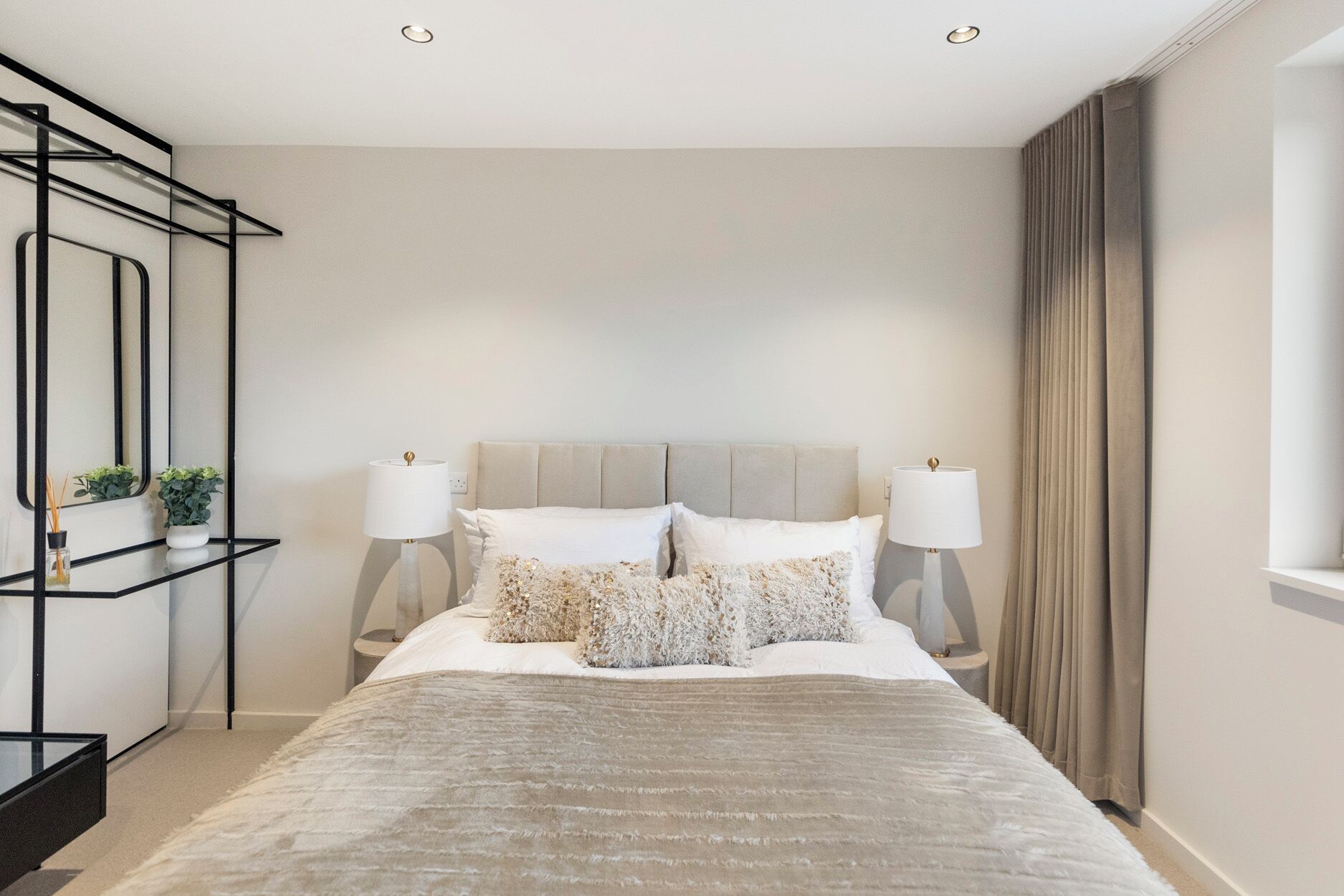 Une chambre moderne avec un grand lit, deux lampes de chevet, un miroir et une petite table agrémentée de plantes.