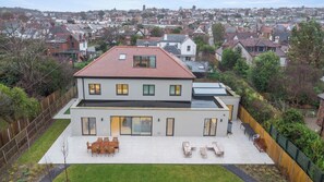 Een modern huis met twee verdiepingen, een plat dak, grote ramen en een ruim terras met buitenmeubilair.