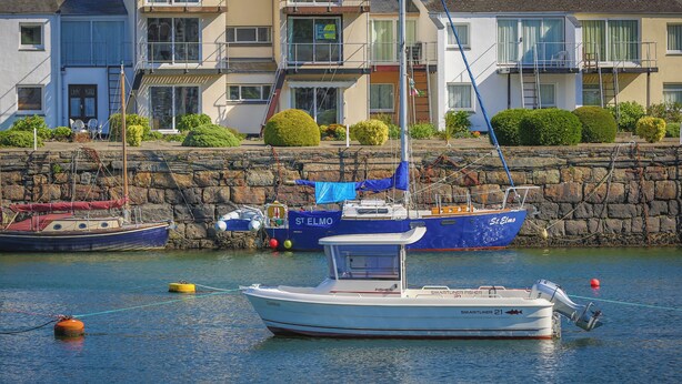 A marina with boats docked, a stone wall, and a row of multi-story buildings with balconies. - 66D South Snowdon Wharf (Porthmadog)