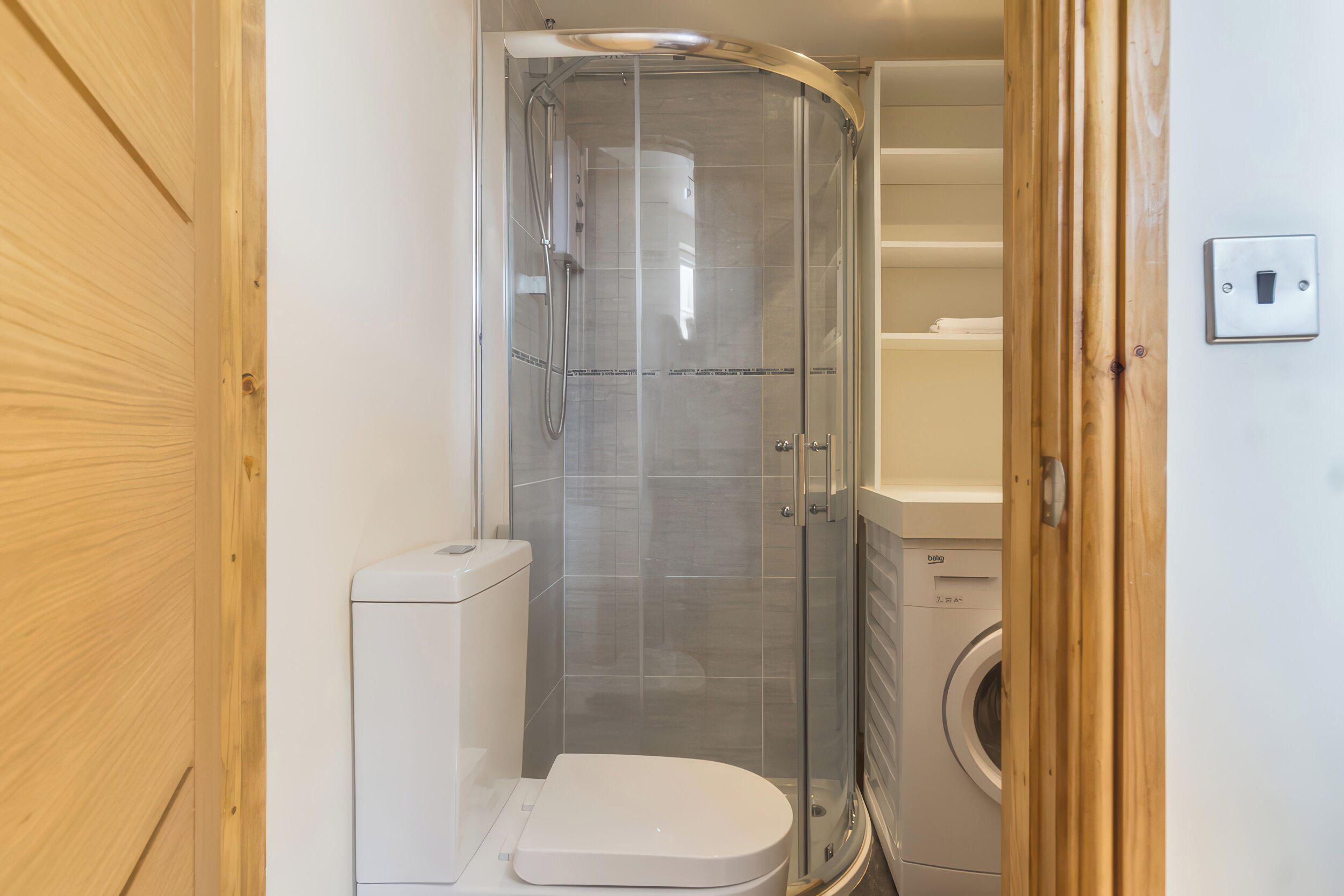 A compact bathroom with a shower enclosure, toilet, and washing machine.