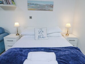 A neatly made bed with white linens, two bedside lamps, a pillow with a quote, a painting on the wall, and a bookshelf with books. - Upper Calffield Studio (Haverfordwest)