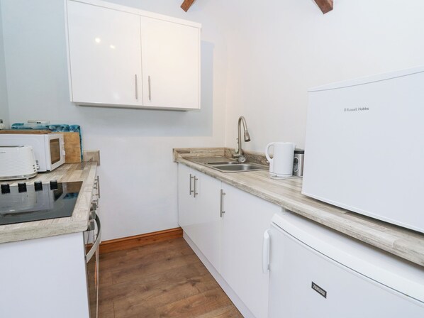 A compact kitchen with white cabinets, a built-in microwave, a stove, and a refrigerator. - Upper Calffield Studio (Haverfordwest)