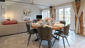 A modern dining area with a round table set for four, surrounded by leather chairs. There is a sofa and a television in the background. - Barley Cottage (Huntingdon)