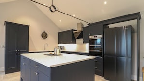 A modern kitchen with dark cabinetry, a large island, stainless steel appliances, and a clock on the wall. - Barley Cottage (Huntingdon)