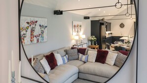 A modern living room with a sectional sofa, a dining area, and a kitchen visible through an open door. - Barley Cottage (Huntingdon)