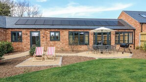 A brick house with a patio, a barbecue, and two beach chairs. - Barley Cottage (Huntingdon)
