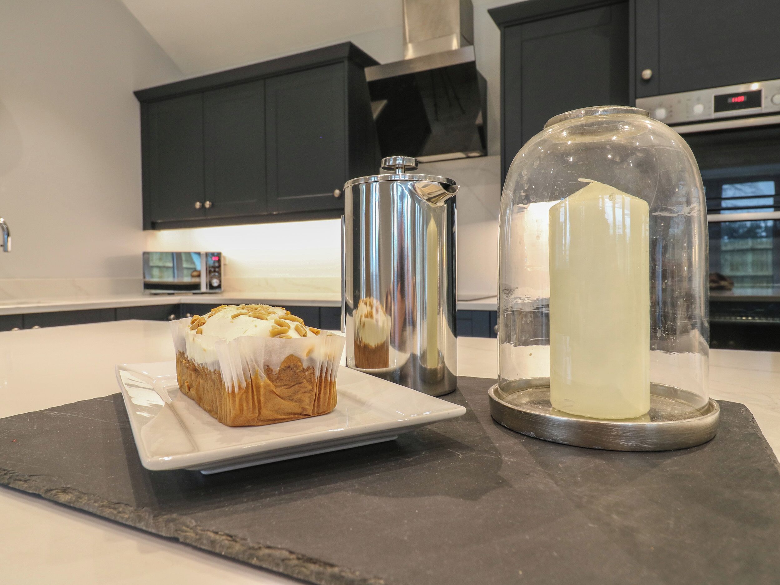 A kitchen counter with a plate of food, a pitcher, and a glass dome.