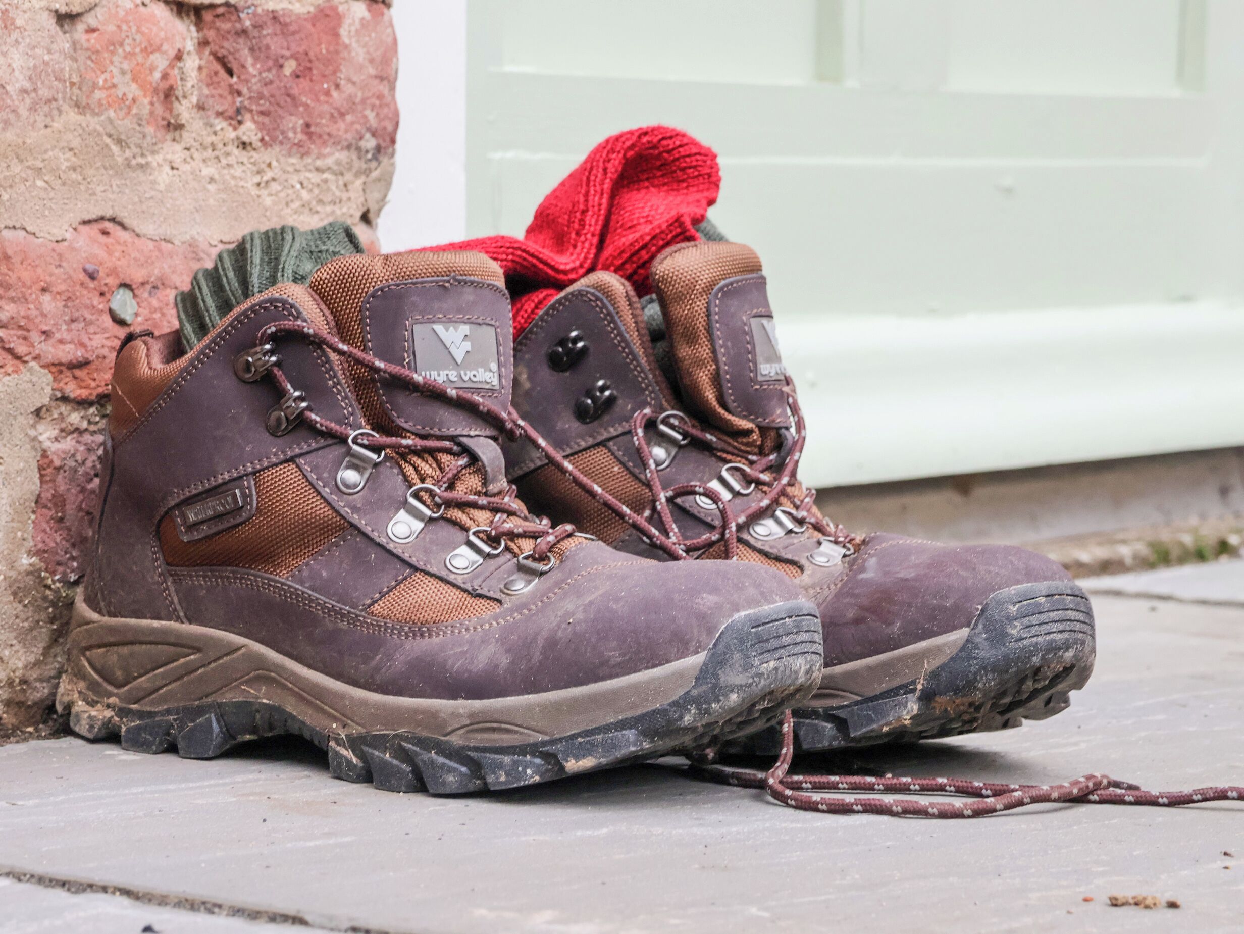 Un par de botas de senderismo con suela resistente y cordones, sobre una superficie de concreto al lado de un muro de ladrillo.
