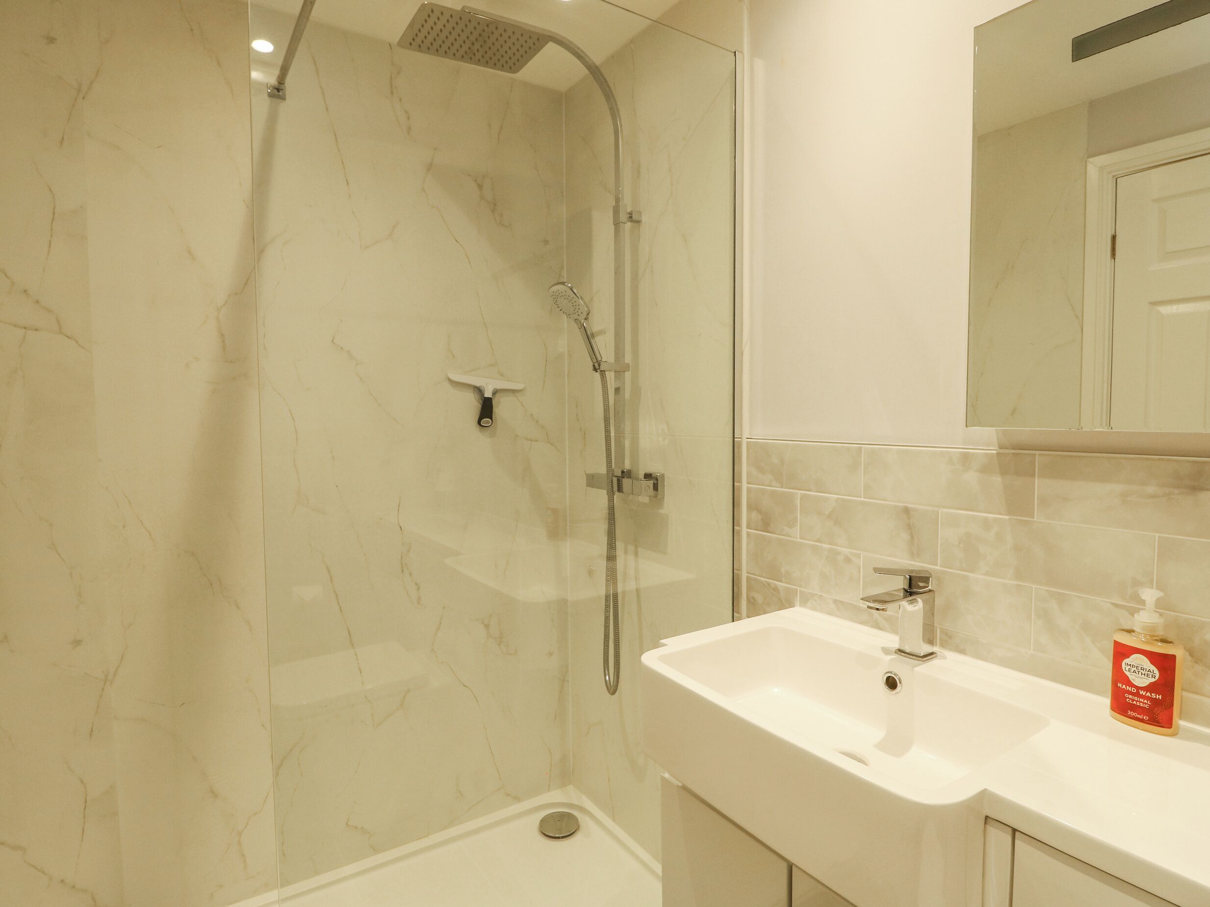 A bathroom with a glass-enclosed shower, a white sink, and a mirror above it.