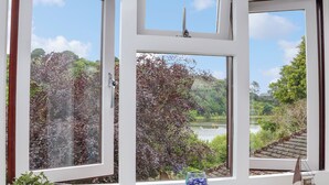 A window with multiple panes, each offering a view of a lush landscape with trees and a body of water. - Squirrels Leap (Falmouth)