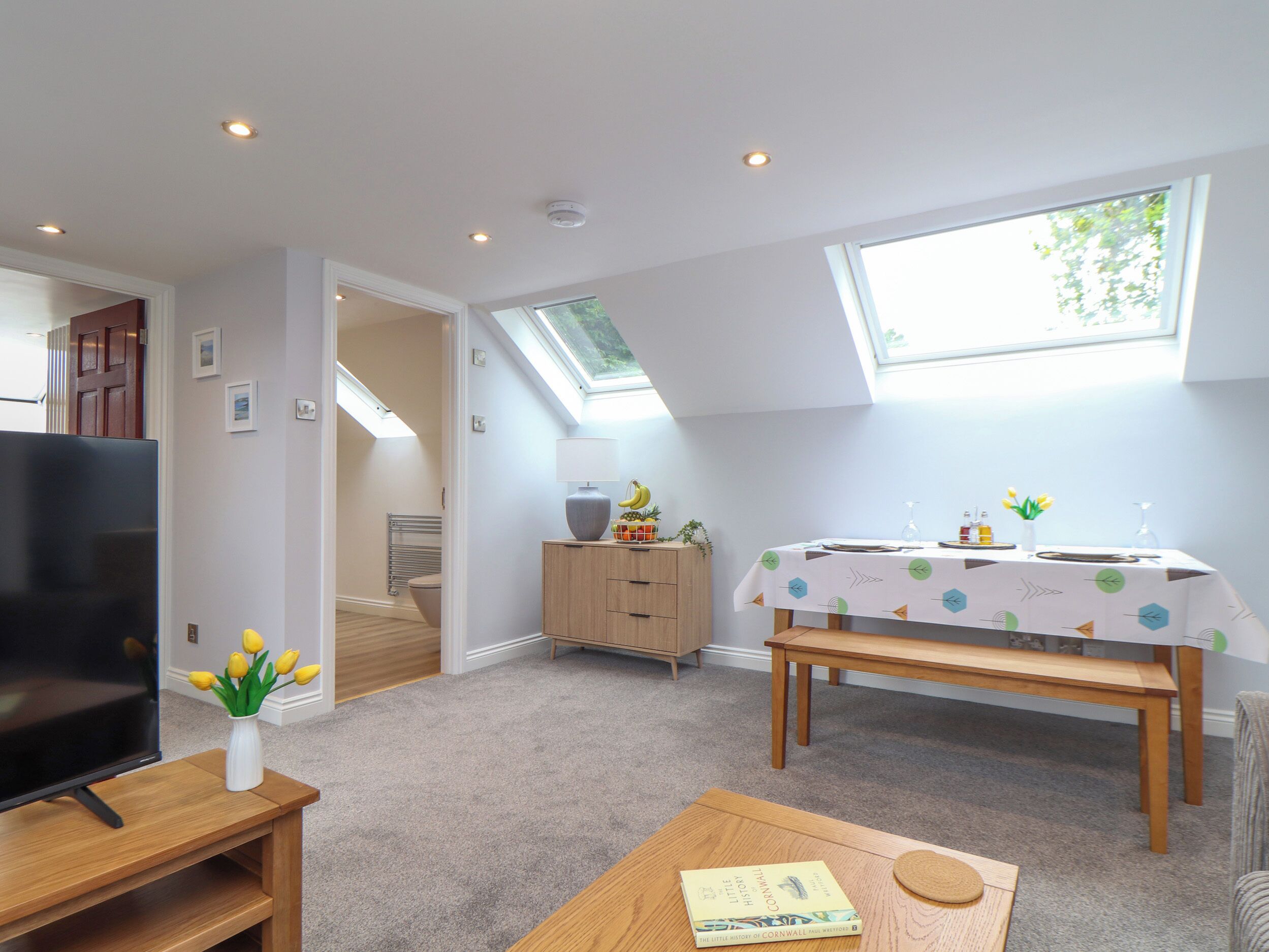 A compact living space with a TV, a dining table with a tablecloth, a bookshelf, and a skylight.