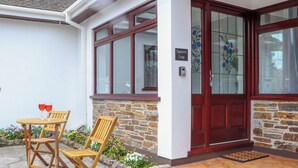 A house with a stone exterior, a red door, and a small garden with flowers and a wooden bench. - Squirrels Leap (Falmouth)