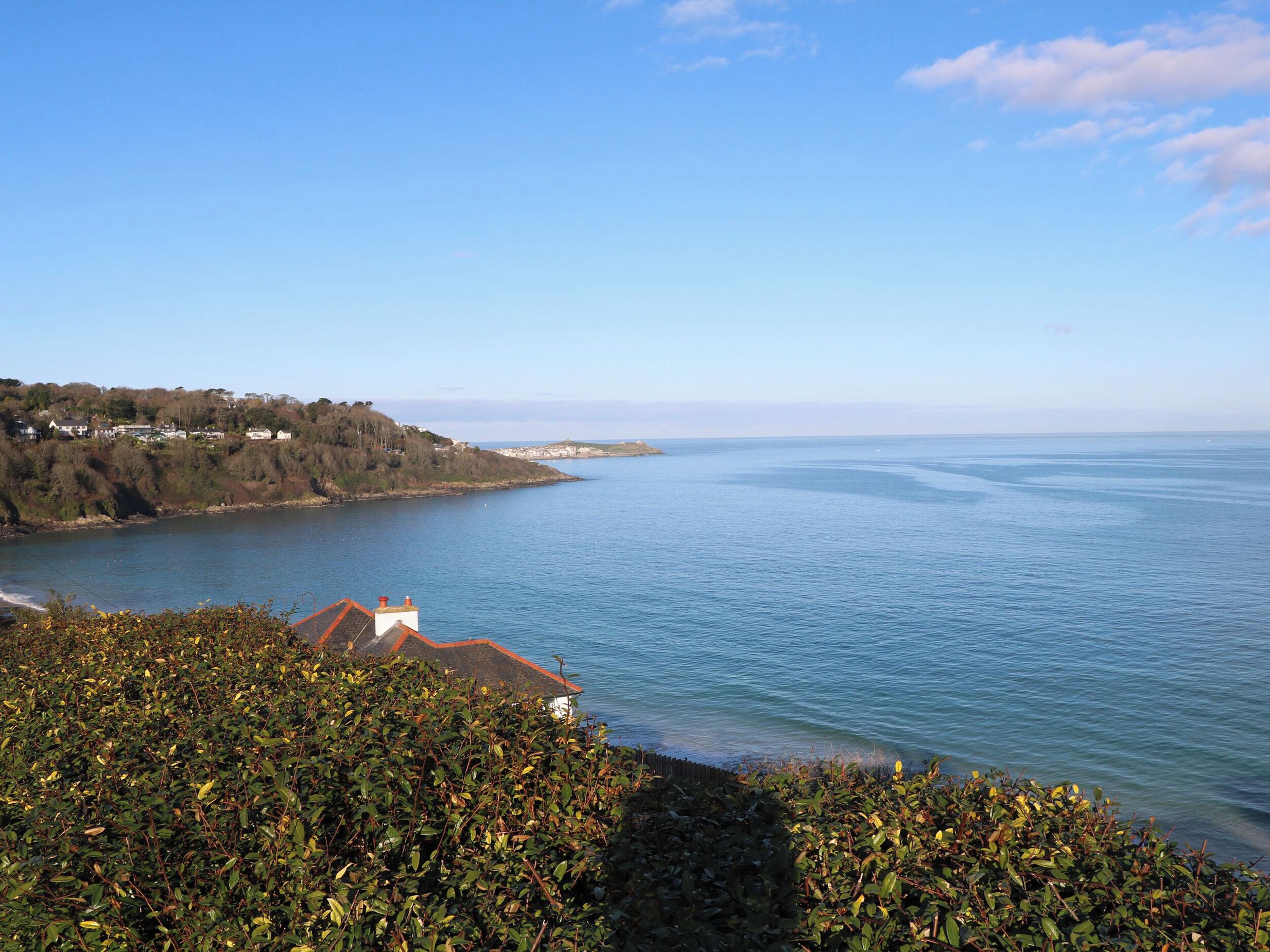 Un paysage côtier avec vue sur la mer, une petite île et un bâtiment doté d’un toit rouge.
