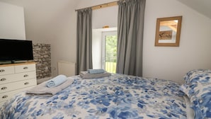 Um quarto com cama, penteadeira, televisão, janela com cortinas e um quadro na parede.