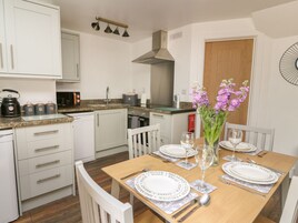 Una cocina moderna con armarios blancos, encimera de granito y comedor para cuatro personas, con mesa, sillas y un jarrón de flores.