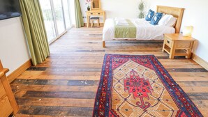 A bedroom with a bed, bedside table, nightstand, wooden floor, and a large window with curtains. - Heron's Den (Horncastle)