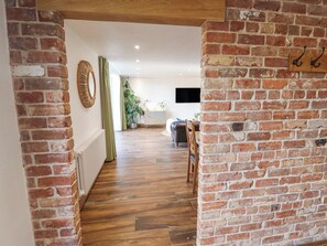 Un pasillo con paredes de ladrillo visto, piso de madera y vista a una sala de estar con sofá y televisor.