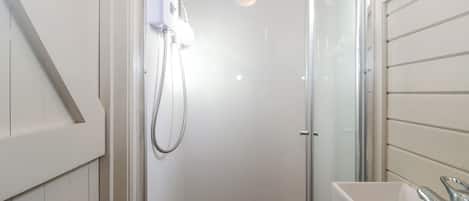 A small, enclosed shower area with a glass door, a white sink with a chrome faucet, and a showerhead mounted on the wall.