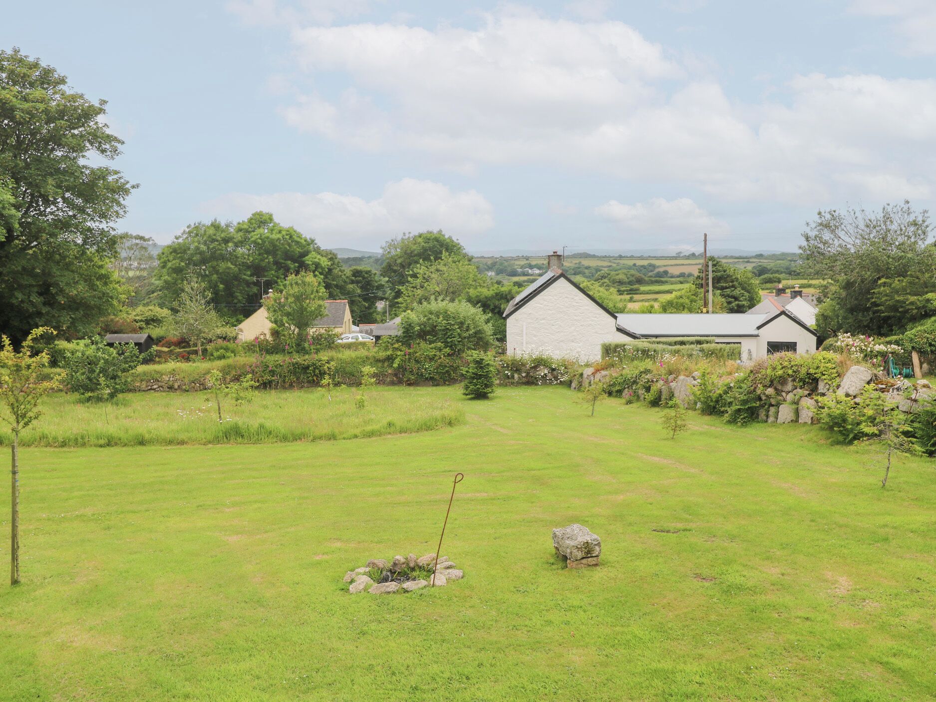 A rural landscape with a stone house, a grassy field, and a stone circle.