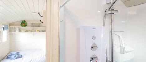 Een moderne badkamer met een douche, toilet en wastafel. Er is een bed met een blauw-wit gestreept laken en een klein plantje op de plank.
