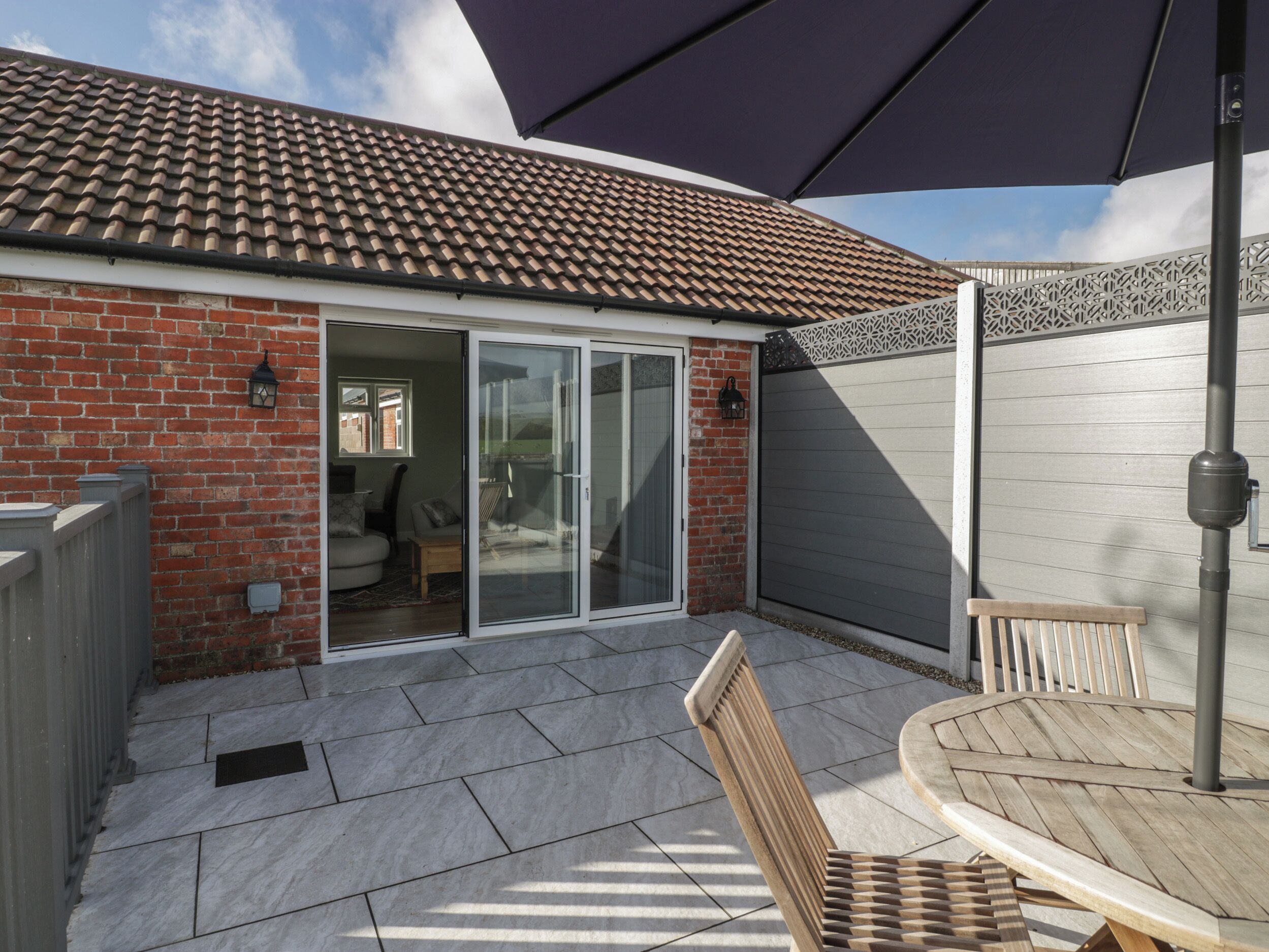 A patio area with a tiled roof, a sliding glass door, a wooden table, and a bench.