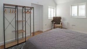 Een slaapkamer met een bed, een stoel, een kledingkast met houten hangers en een raam met jaloezieën.